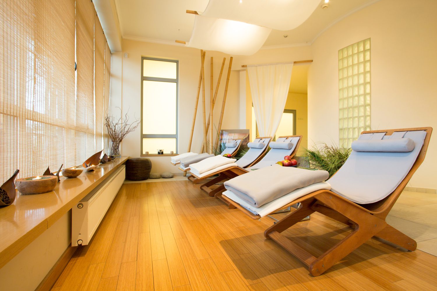 An image of a relaxing spa room with wooden lounge chairs, bamboo blinds, and soft lighting.